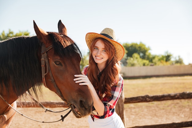 Porträt des lächelnden schönen jungen Frauenkuhmädchens mit ihrem Pferd auf Bauernhof