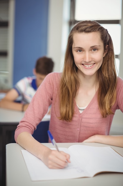 Porträt des lächelnden Schulmädchens, das Hausaufgaben im Klassenzimmer macht