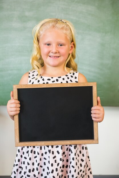 Porträt des lächelnden Schulmädchens, das Tafel im Klassenzimmer hält