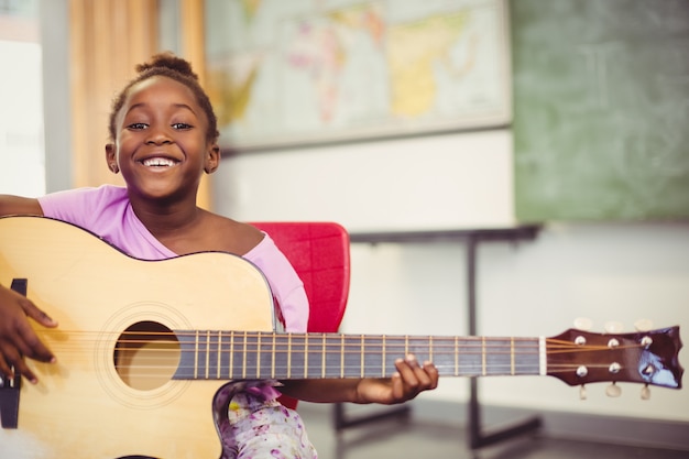 Porträt des lächelnden Schulmädchens Gitarre im Klassenzimmer spielend