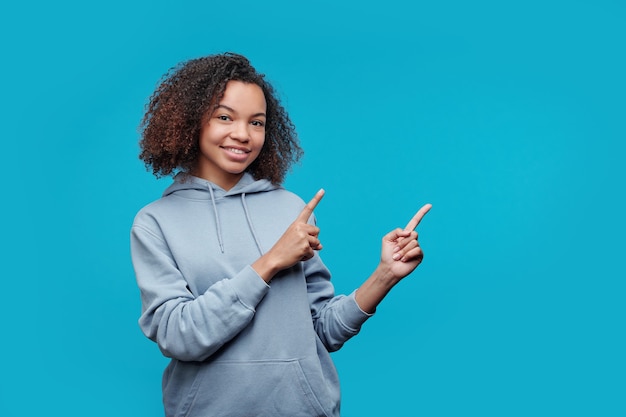 Porträt des lächelnden schwarzen Studentenmädchens mit Afro-Frisur, die beiseite gestikuliert, während Online-Kurs oder pädagogisches Info-Produkt empfohlen