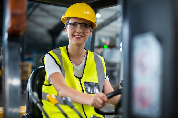 Porträt des lächelnden weiblichen Fabrikarbeiters, der Gabelstapler fährt