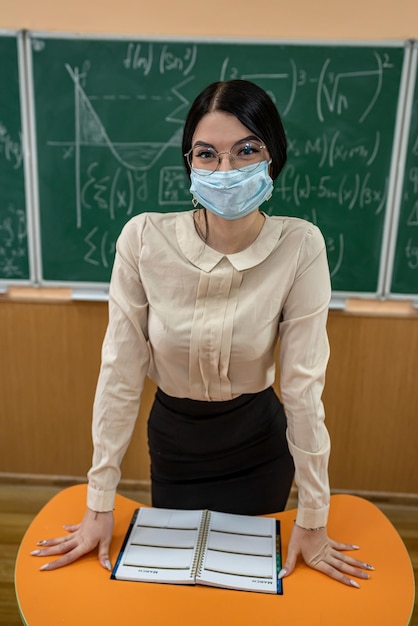 Porträt des Lehrers in medizinischer Maske während der Coronavirus-Epidemie, der an der Tafel steht