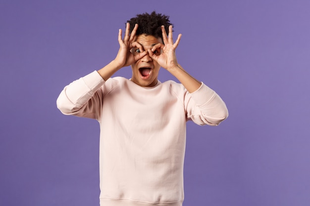 Porträt des lustigen, enthusiastischen jungen hispanischen Mannes, der herumalbert und Fingerbrille macht