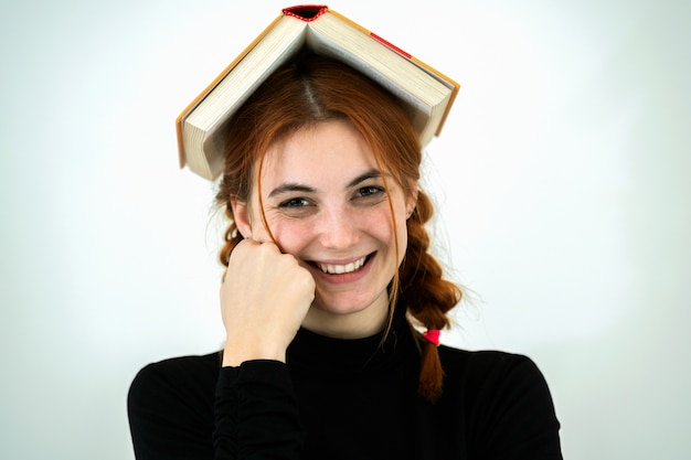 Porträt des lustigen jungen lächelnden Studentenmädchens mit einem offenen Buch auf ihrem Kopf. Lese- und Bildungskonzept.