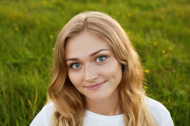 Porträt des Mädchens, das nettes Lächeln mit Grübchen auf ihrem Gesicht hat, das weißes T-Shirt auf Grün trägt