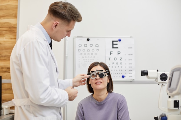 Porträt des männlichen Augenoptikers, der Versuchrahmen auf weibliche Patientin setzt