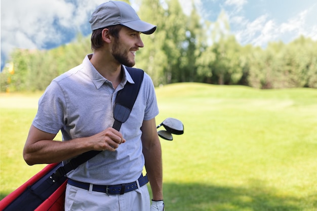 Porträt des männlichen Golfspielers, der Golftasche beim Gehen durch grünes Gras des Golfclubs trägt.