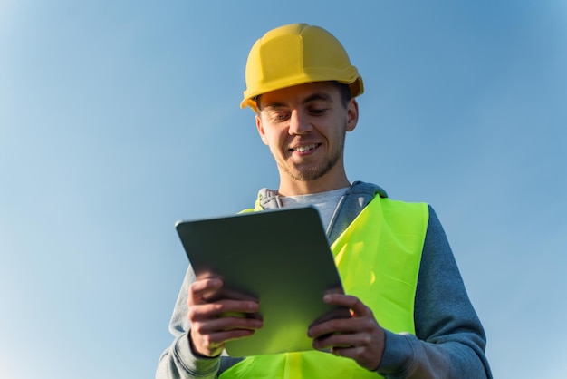 Porträt des männlichen Ingenieurs, der an einem sonnigen Tag während der Arbeit auf dem Solarpark ein Tablet zur Fernsteuerung von Photovoltaikmodulen verwendet