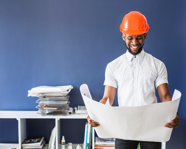 Porträt des männlichen Ingenieurs einen orange Hardhat tragend, der Plan betrachtet