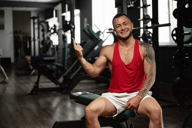 Porträt des Mannbodybuilders im roten Hemd in der Turnhalle