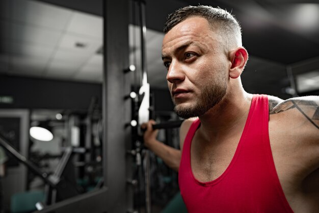 Porträt des Mannbodybuilders im roten Hemd in der Turnhalle