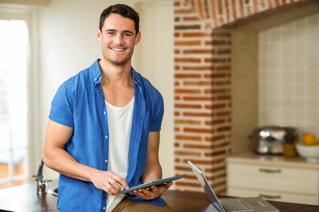 Porträt des Mannes, der digitale Tablette mit Laptop in der Küche verwendet