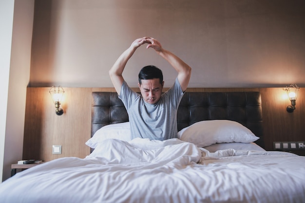 Porträt des Mannes, der im Wachzustand im Bett sitzt und seine Arme ausstreckt