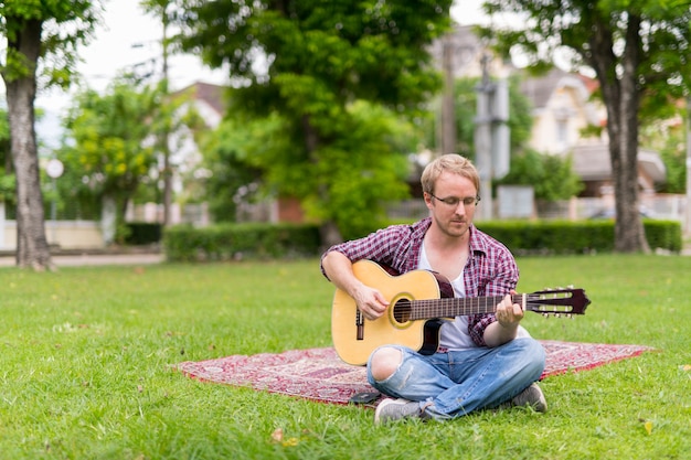 Porträt des Mannes, der Picknick beim Spielen der Gitarre im Freien hat