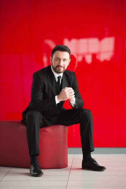 Porträt des Mannes im schwarzen Anzug sitzt auf rotem Sitz