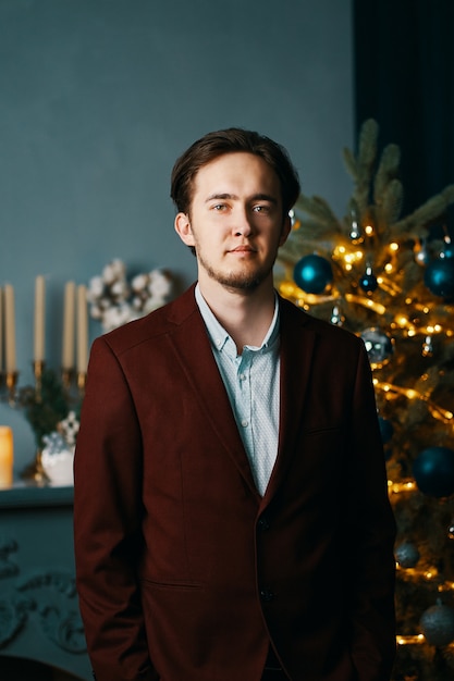 Porträt des Mannes in kastanienbraunem Anzug und Hemd. Weihnachtsbaum und Dekorationen
