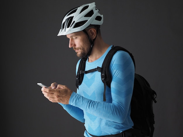 Porträt des Menschen Radfahrer mit Rucksack verwendet Smartphone vor der Fahrt. Grauer Hintergrund.