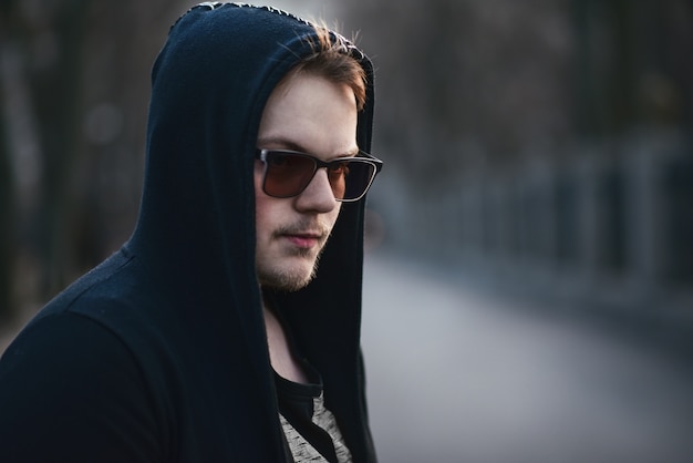 Porträt des Mode-Mannes in einem schwarzen Pullover mit Kapuze und Sonnenbrille
