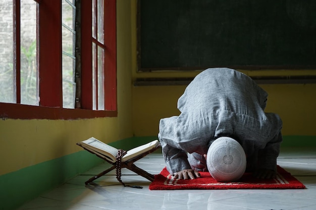 Porträt des muslimischen Mannes Sujud oder Niederwerfung in einer Sajdah mit Koran und Tasbih daneben