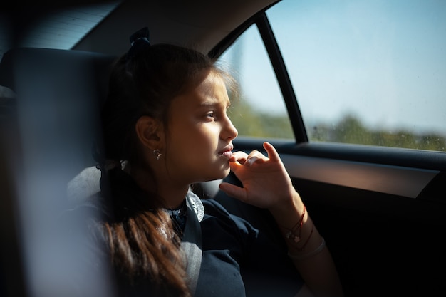 Porträt des nachdenklichen Kindermädchens, das durch Autofenster nach der Schule schaut.