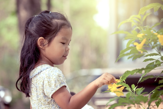 Porträt des netten asiatischen kleinen Mädchens mit gelber Blume im Garten im Weinlesefarbton