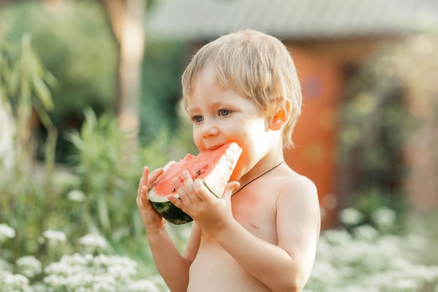 Porträt des netten hübschen in der Natur lustigen Kindes, das Wassermelone isst