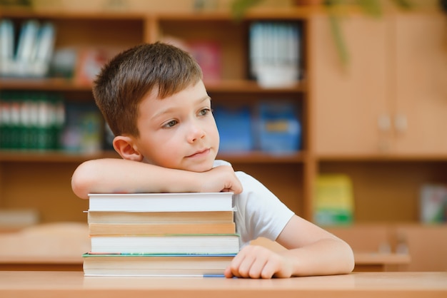 Porträt des netten Jungen auf Buchstapel. Das Konzept des Lernens in der Grundschule.