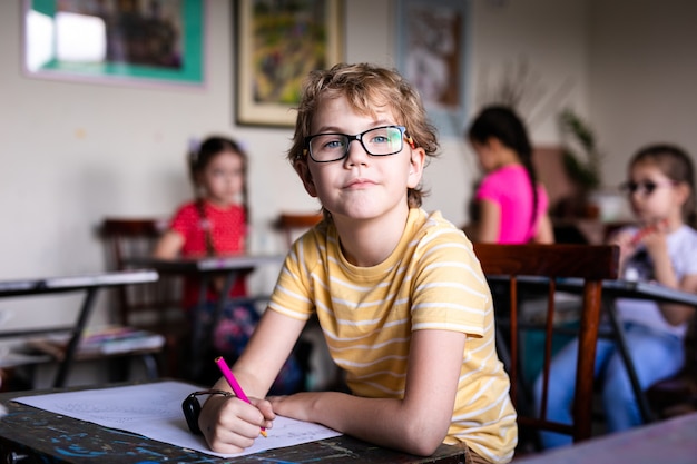 Porträt des netten Jungen mit Skizzenstift und -papier am Schreibtisch im Klassenzimmer.