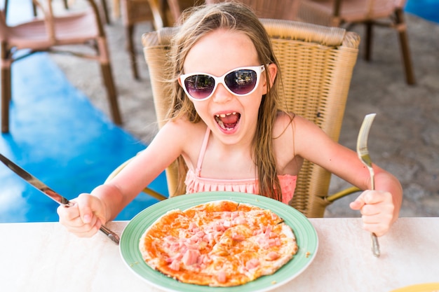 Porträt des netten kleinen Mädchens, das durch Abendtische sitzt und Pizza isst