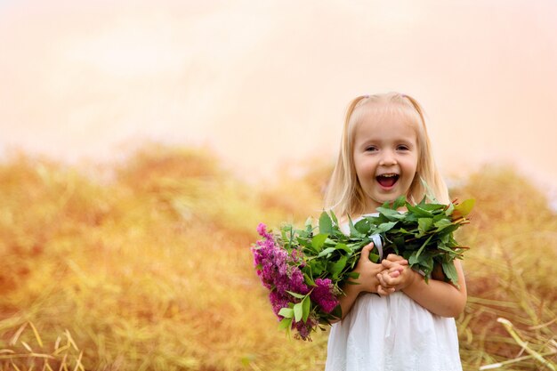 Porträt des netten kleinen Mädchens das Händchenhaltenblumenstrauß von rosa Blumen auf einem Feld