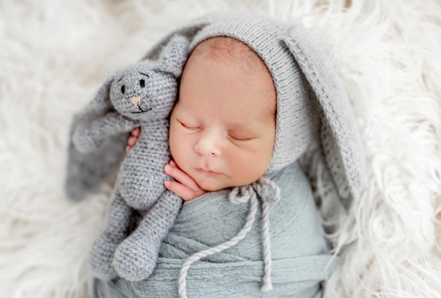 Porträt des Neugeborenen, der schlafendes und gestricktes Häschenspielzeug in den Händen schläft und hält