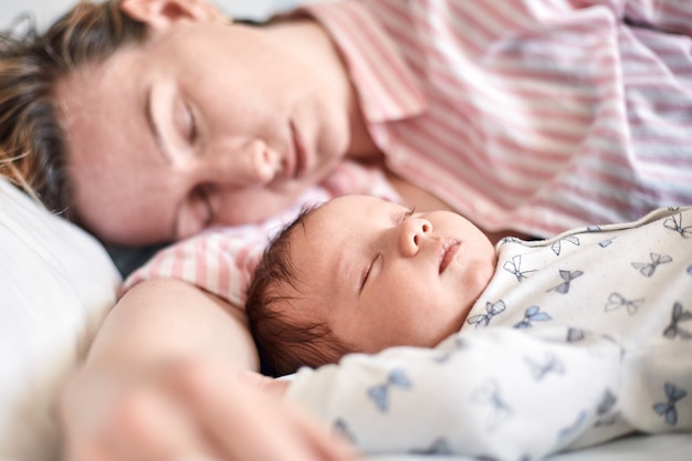 Porträt des Neugeborenen und der Mutter, die auf Bett schlafen und zusammen ruhen