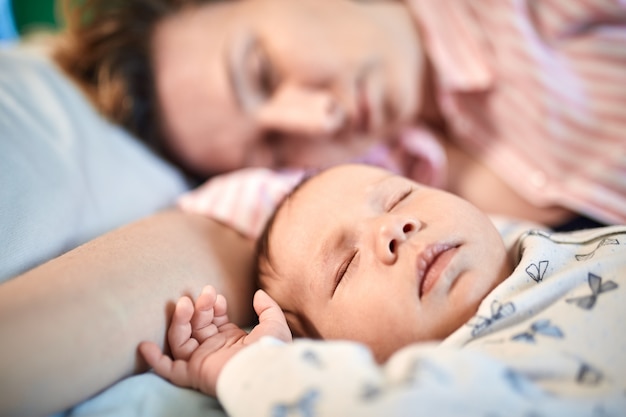 Porträt des Neugeborenenbabys und der Mutter, die auf Bett schlafen