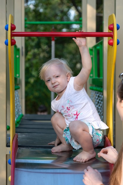 Porträt des niedlichen blonden Kindes im Spielplatz. Barfußkind auf einer Rutsche. Vertikaler Rahmen.
