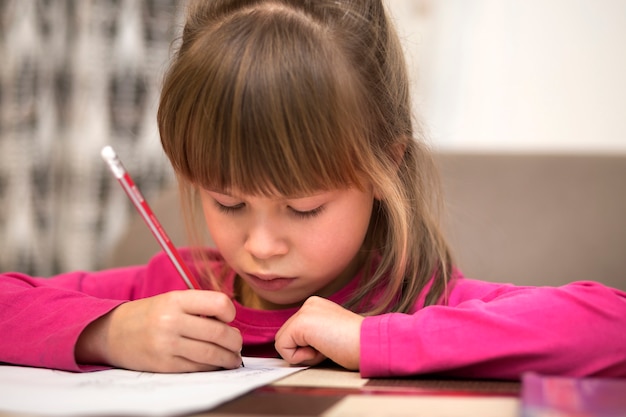 Porträt des niedlichen hübschen kleinen ernsten Kindermädchens, das mit Bleistift auf Papier zeichnet. Kunstvermittlung, Kreativität, Hausaufgaben und Kinderaktivitäten Konzept.