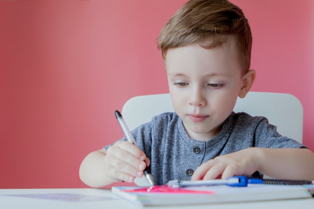 Porträt des niedlichen Kinderjungen zu Hause, der Hausaufgaben macht. Kleines konzentriertes Kind, das mit buntem Bleistift drinnen schreibt. Grundschule und Bildung.