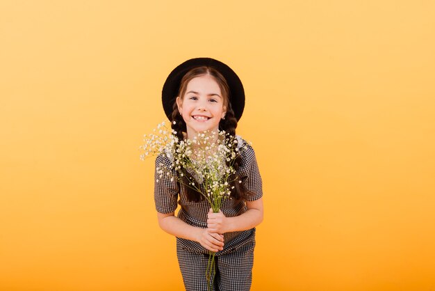 Porträt des niedlichen kleinen Mädchens mit Blumenstrauß im Studio auf gelbem Hintergrund. Herzlichen Glückwunsch, Frühling oder fröhliches Urlaubskonzept. Kopieren Sie Platz für Text