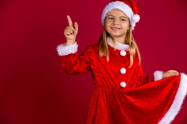 Porträt des niedlichen Mädchens im Weihnachtsmannkostüm und in der Wintermütze. Kind hält das rote Kleid von Hand und