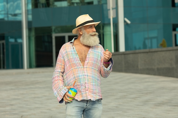 Porträt des positiven älteren bärtigen Hipster-Mannes, der Kaffeepause im Freien auf städtischen Einstellungen hat.