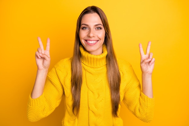 Porträt des positiven fröhlichen Mädchens haben Winterwochenenden machen V-Zeichen genießen Freizeit tragen weiche warme Kleidung über helle Farbe Wand isoliert