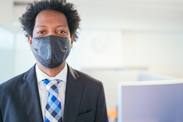 Porträt des professionellen Geschäftsmannes, der Gesichtsmaske trägt, während am modernen Büro steht. Neuer normaler Lebensstil. Unternehmenskonzept.