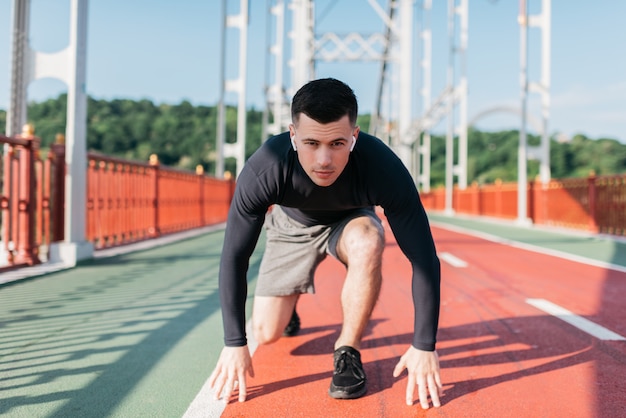 Porträt des professionellen Läufers am Start bereit zum Sprint. Sportmann, der Musik mit drahtlosen Kopfhörern im Freien hört