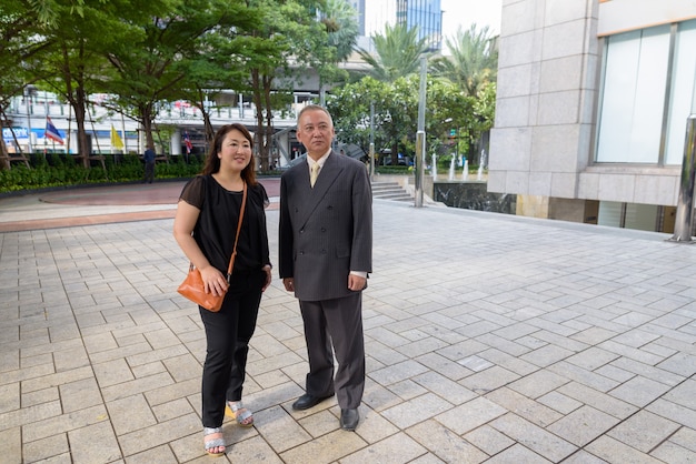 Porträt des reifen japanischen Geschäftsmannes und der reifen japanischen Frau, die die Stadt Bangkok erkunden