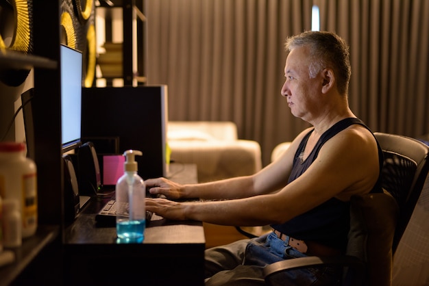 Porträt des reifen japanischen Mannes, der Computer zu Hause benutzt