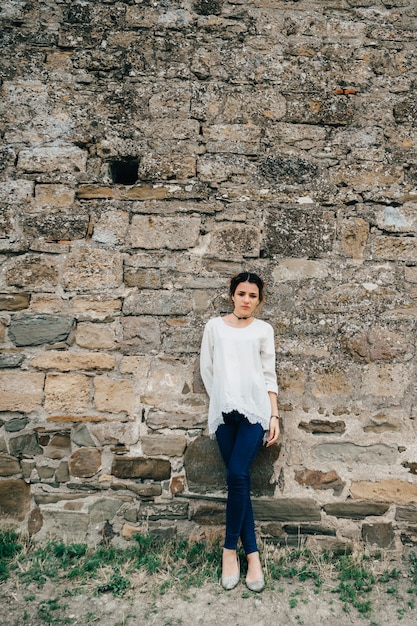 Porträt des reisenden Mädchens im weißen Kleid steht an der alten Steinmauer