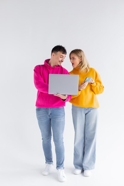 Porträt des reizenden Mannes und der Frau, die silbernen Laptop halten, während sie lokalisiert über weißem Hintergrund stehen