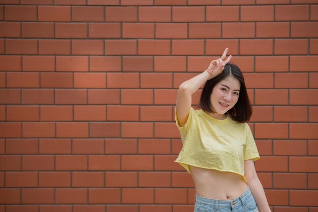 Porträt des schönen asiatischen schicken Mädchens, das für ein Foto auf der Ziegelwand posiertLifestyle of teen thailand peopleModern woman happy concept