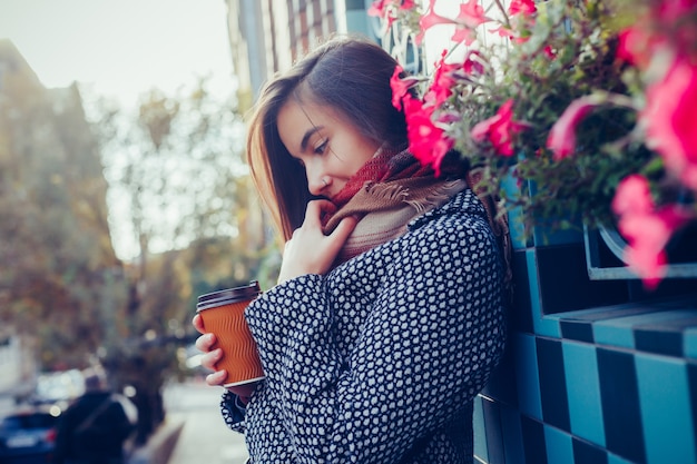 Porträt des schönen Brunettemädchens mit Getränk zum Mitnehmen auf der Straße. Schal und Herbstmantel in der Stadt. Erstaunliche Aussicht auf eine Geschäftsfrau mit einer Tasse Kaffee, die die Stadtstraße hinuntergeht.