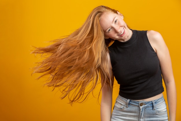 Porträt des schönen fröhlichen rothaarigen Mädchens mit dem fliegenden Haar, das über gelbe Wand lachend lächelt